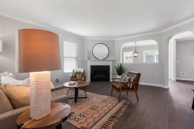 Listing photo of a living room with a corner fireplace, a round mirror, a window, an arched pass-through to the dining room and an arched doorway