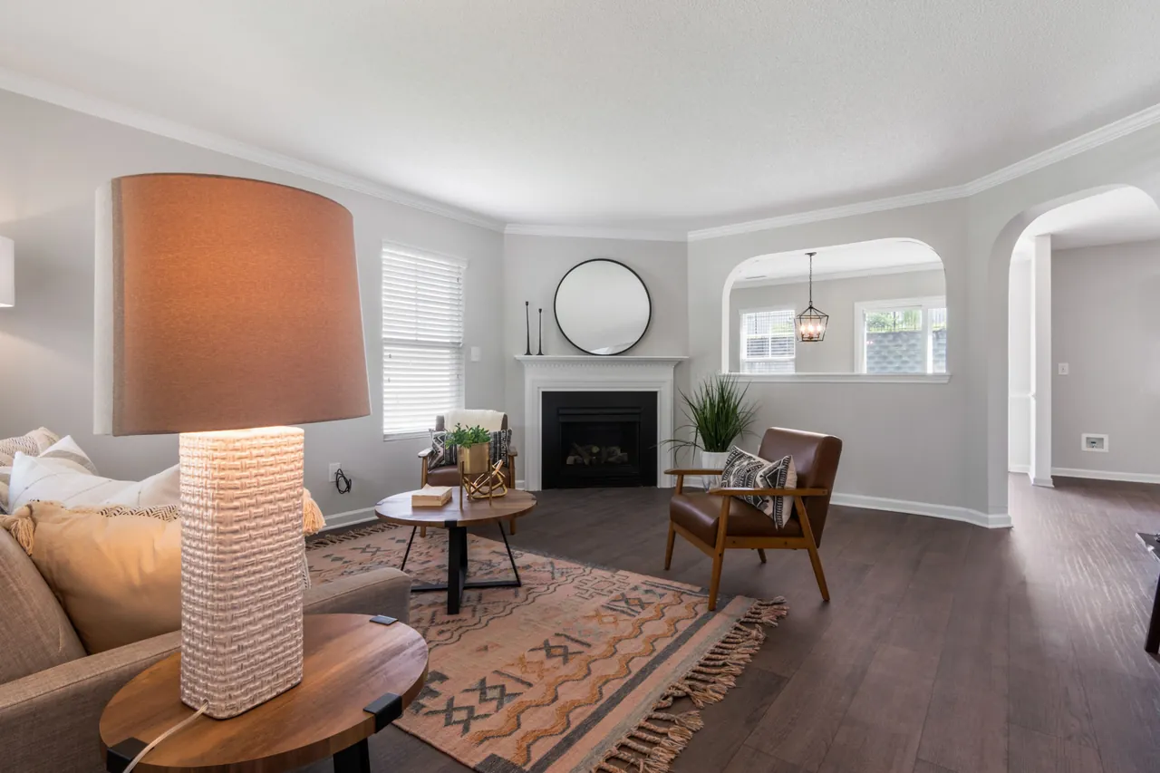 Listing photo of a living room with a corner fireplace, a round mirror, a window, an arched pass-through to the dining room and an arched doorway